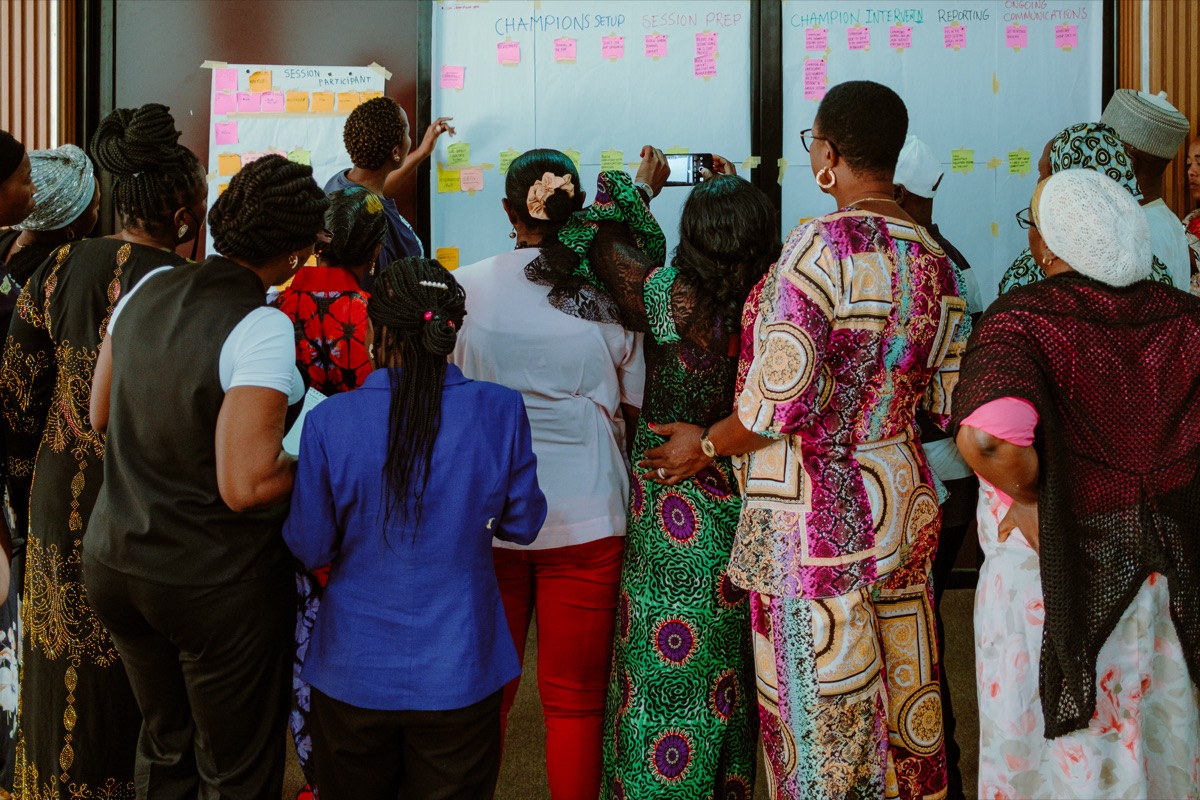 Workshop participants reviewing a wall of sticky notes mapping the Champions programme setup and session prep.