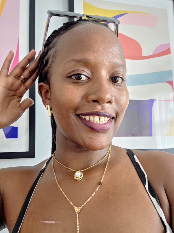 Black-and-white portrait of Diana Wambui smiling, glasses pushed up on her head.