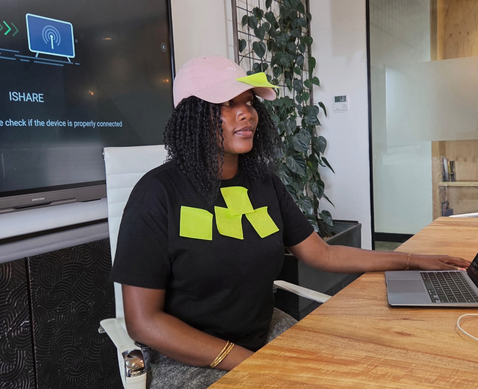 Diana at a desk working on a laptop, wearing a cap and a graphic tee.